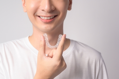 Young smiling man holding invisalign braces over white background