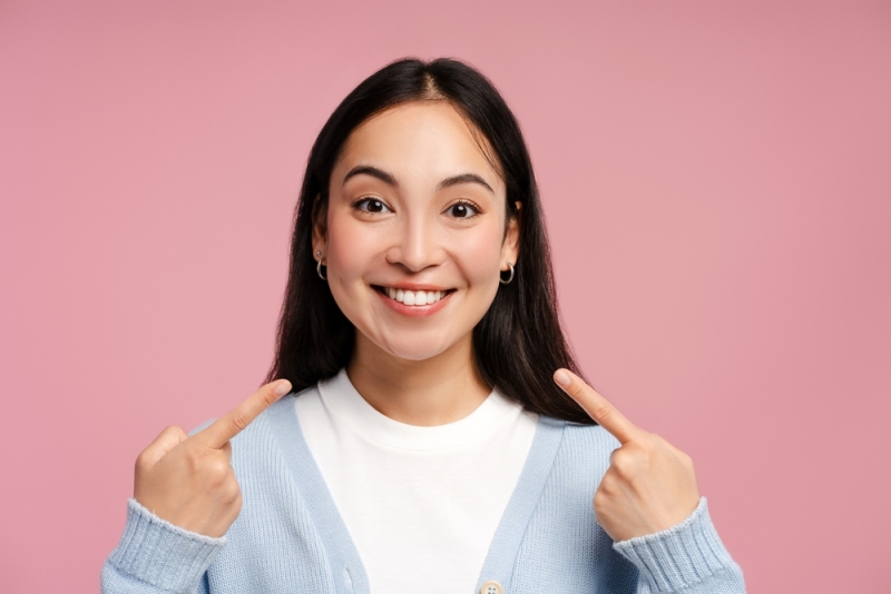 Woman smiling and pointing to teeth with dental bridge in Calgary, CA