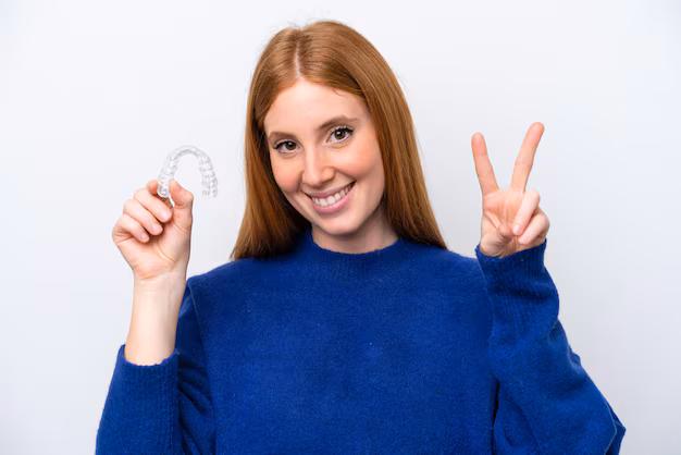 young-redhead-woman-holding-invisible-braces-isolated-white-background-smiling-showing-victory-sign